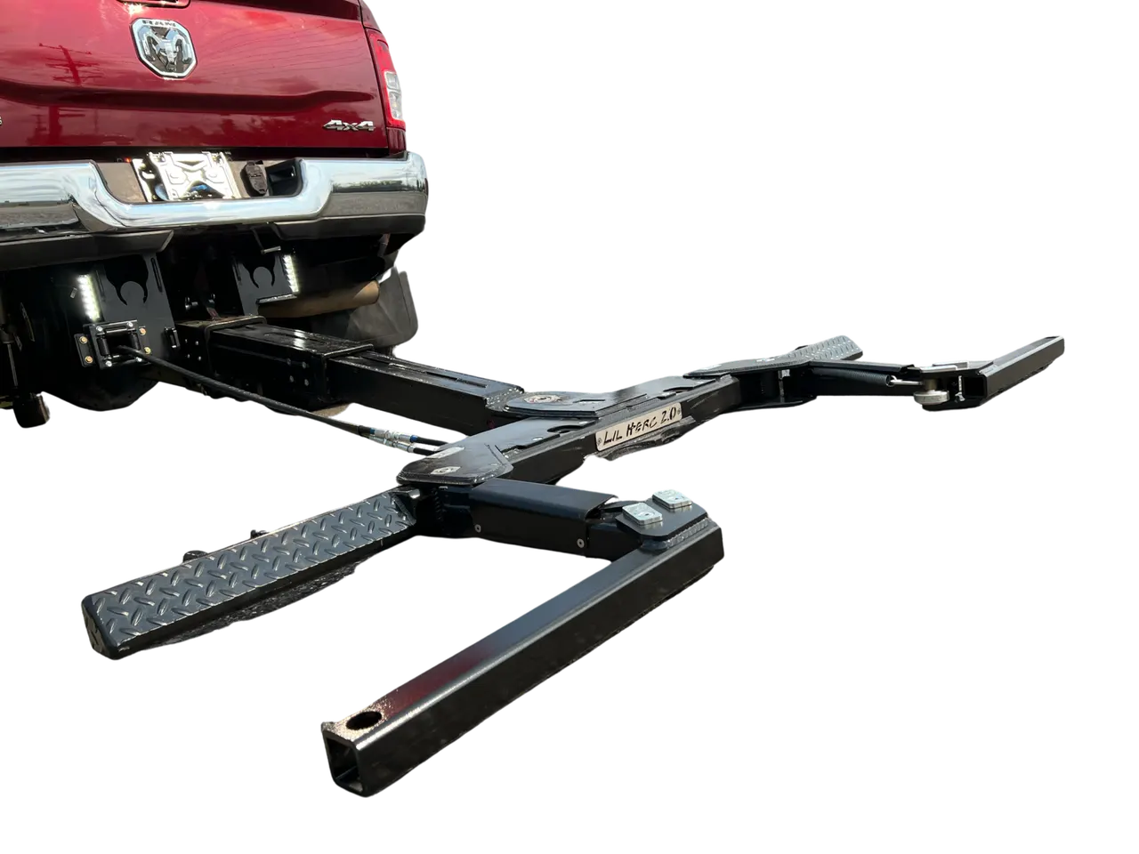 Lil Hercules 2.0 wheel lift extended beneath a red pickup, showing its stinger, crossbar, and L-arms