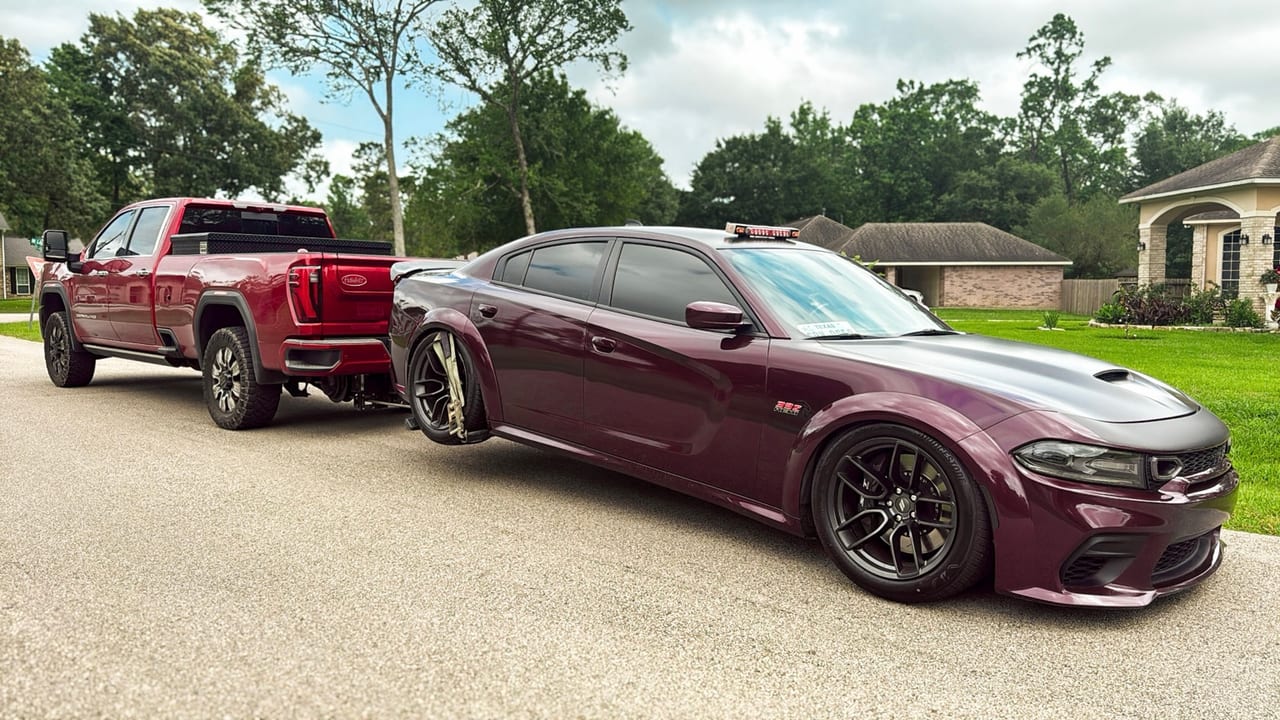Red pickup towing a burgundy Dodge Charger with a sneaker wheel lift